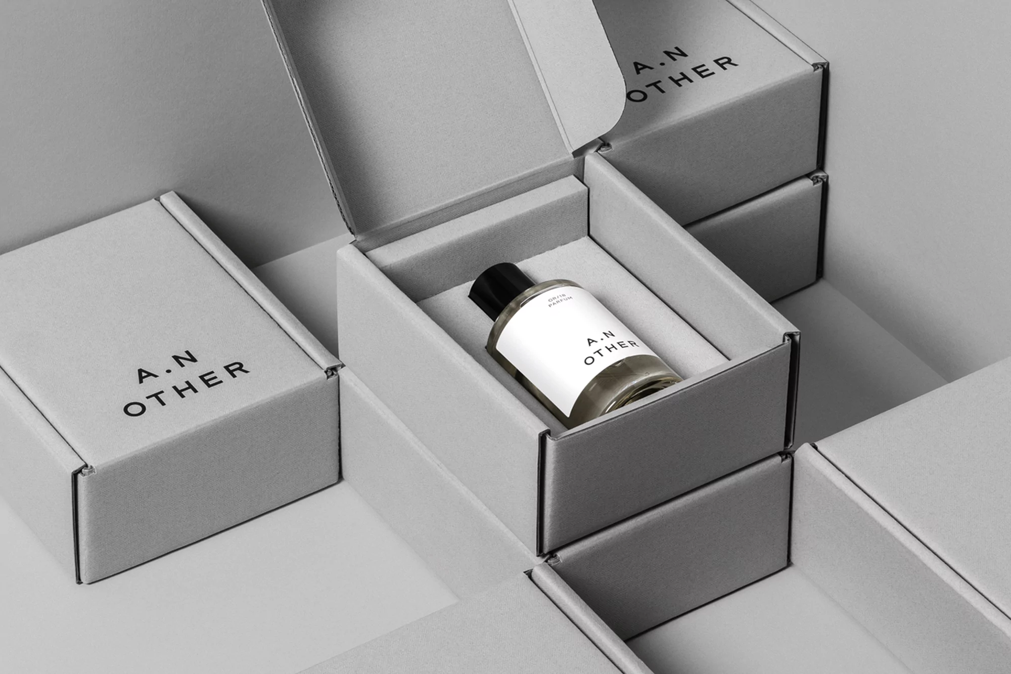 A.N Other perfume bottle in an open grey branded packaging box surrounded by stacked boxes.