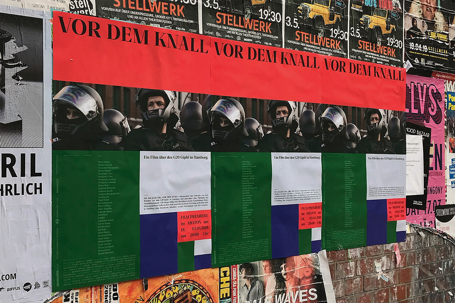 Multiple posters on a brick wall feature a row of people in riot gear beneath the text 'Vor Dem Knall', next to other posters.