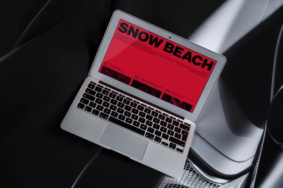 Laptop with Snow Beach website display, resting on a dark, textured surface, under direct lighting, showcasing a clean, modern design.