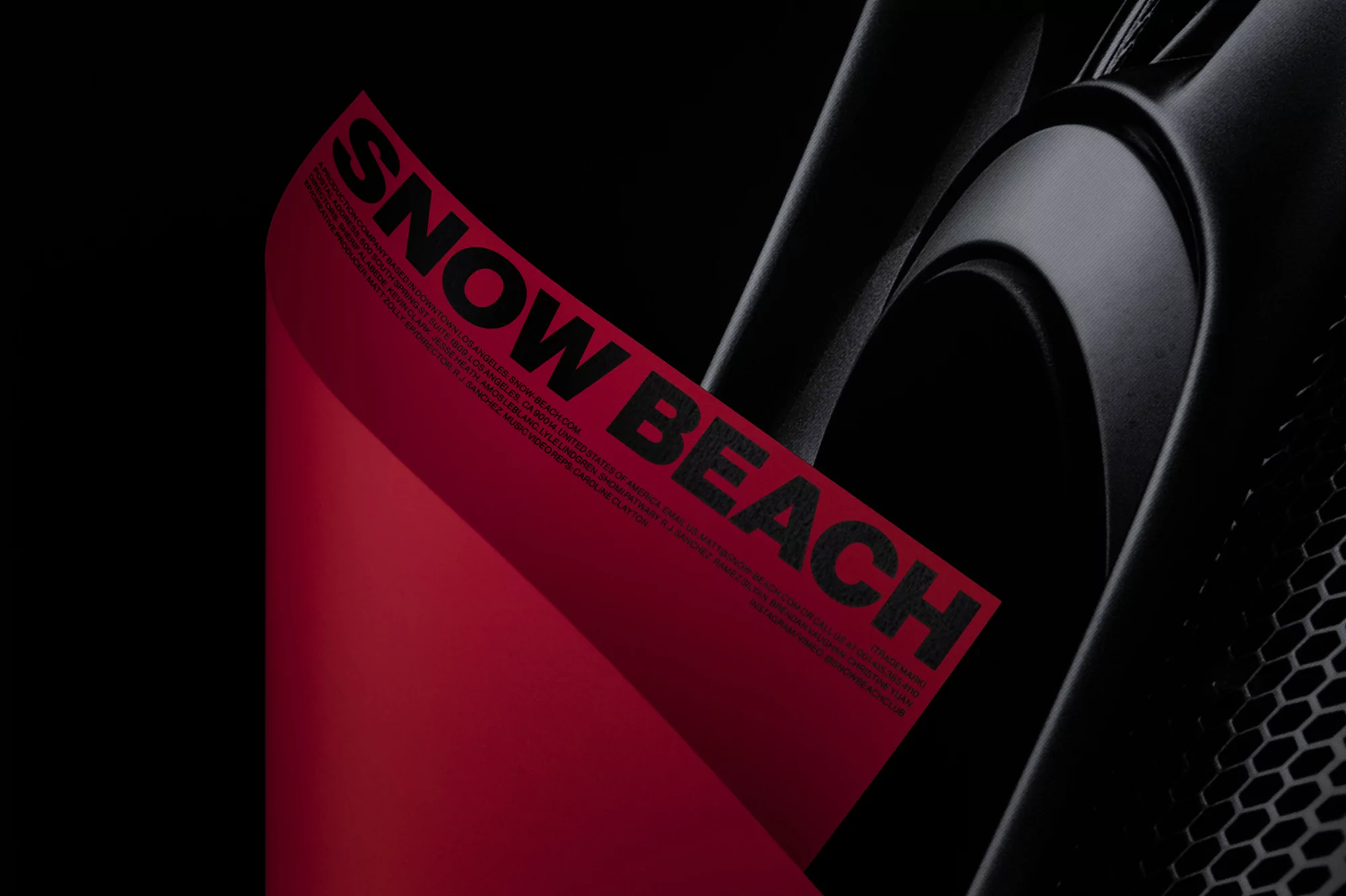 A close-up shot of a sleek, black bicycle frame with a vibrant red paper attached, featuring the text 'SNOW BEACH' in bold, black letters.