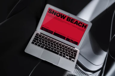 Silver laptop displaying Snow Beach branding on a bright red screen, resting on a dark automotive interior.