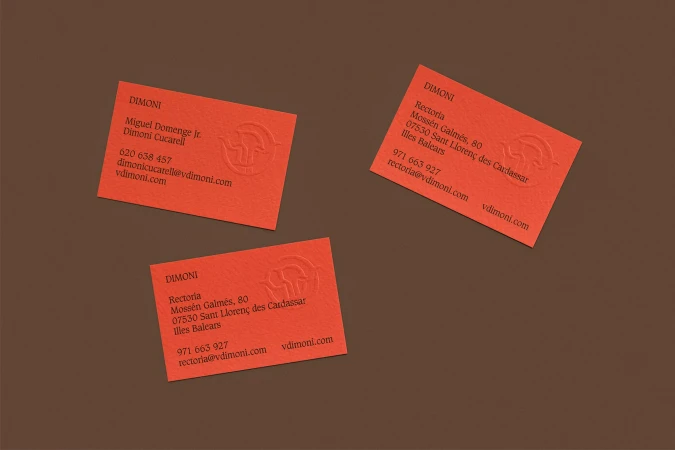 Three orange business cards with logo and contact information, scattered on a brown background, promoting a professional brand identity.