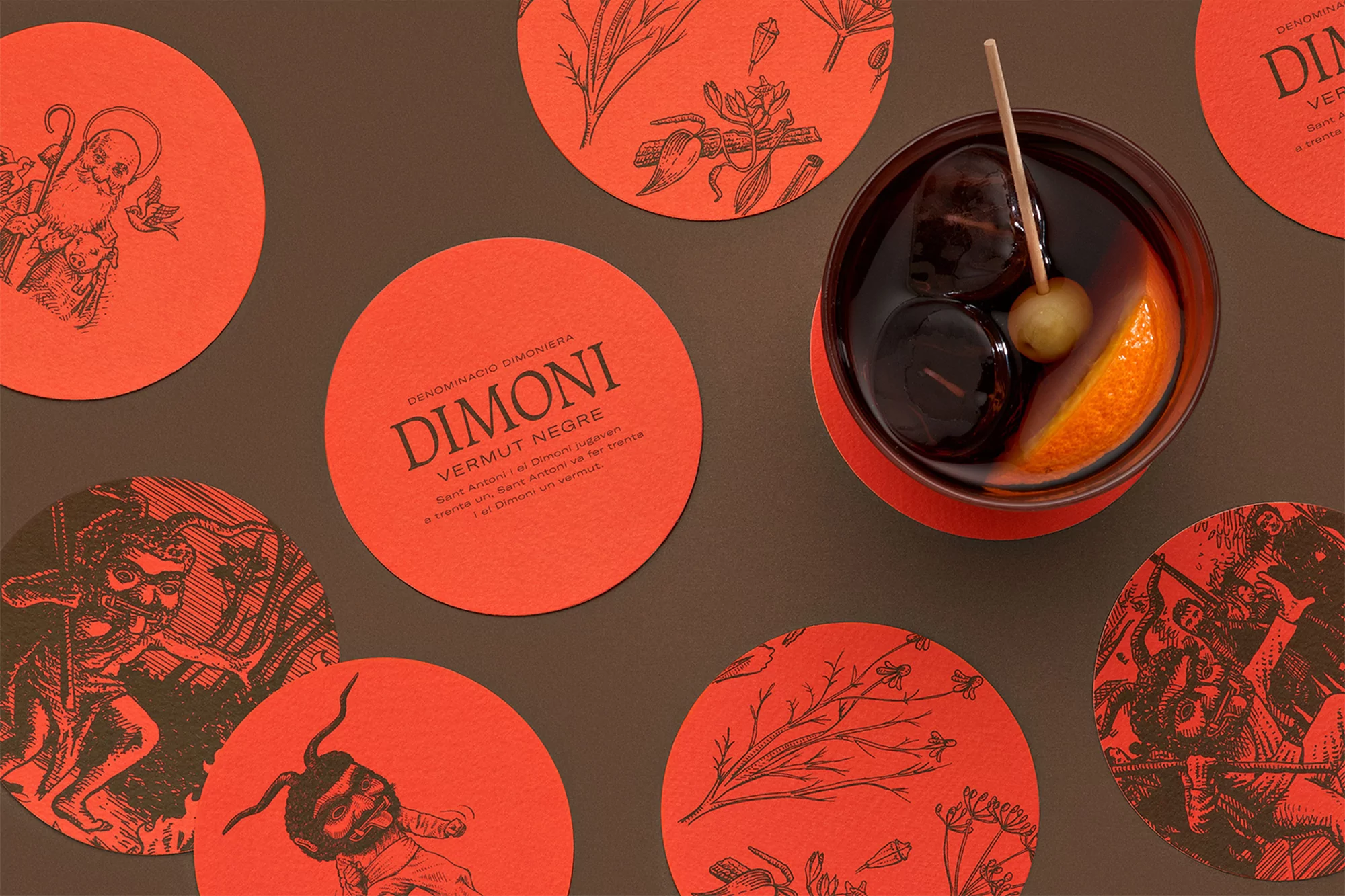 Overhead shot of a cocktail drink with an orange slice, dark cherries, and a green olive, surrounded by red Dimoni vermouth coasters.