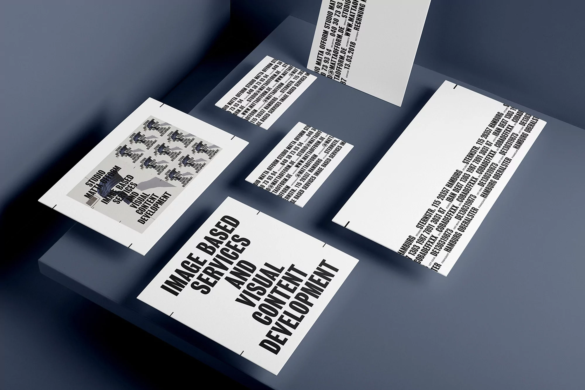 Eye-level shot of studio promotion with flyers and business cards. Flyers feature black text on a white background, displayed on a grey background.