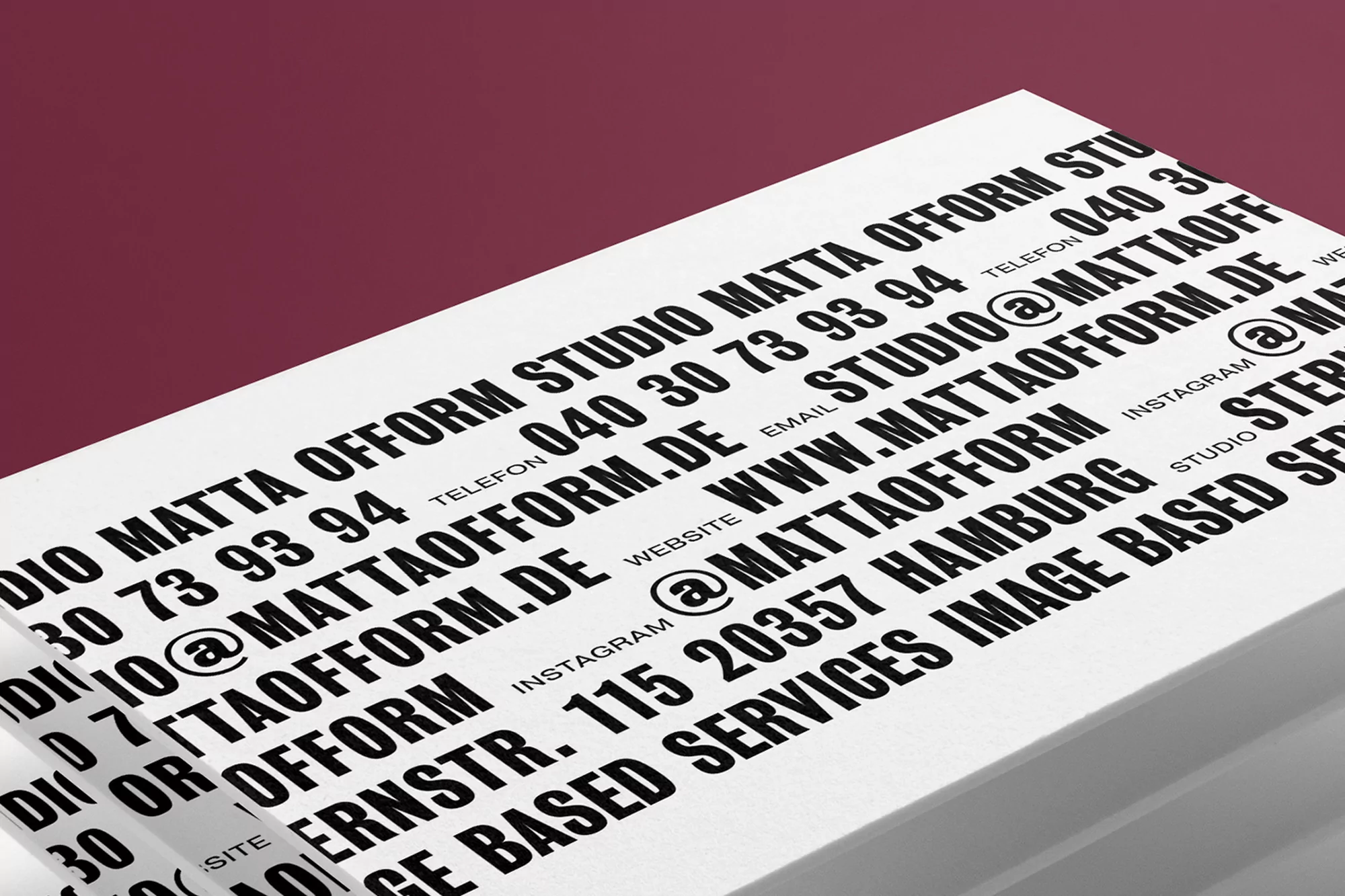 Close-up of stacked white cards with black text displaying 'MATTA OFFORM STUDIO' contact information against a maroon background.