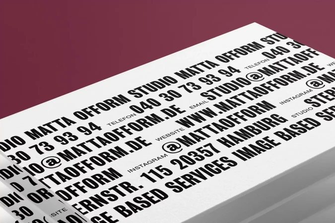 Close-up of stacked white cards with black text displaying 'MATTA OFFORM STUDIO' contact information against a maroon background.
