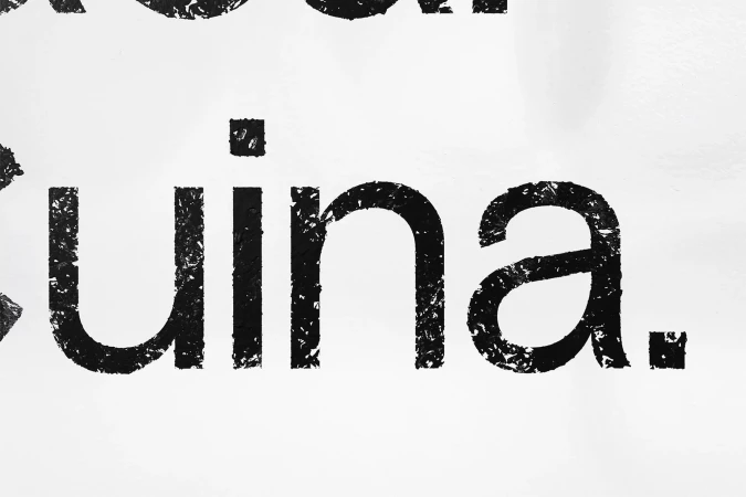 Close-up of black textured text spelling 'Cuina' on a white background. The text is stylized with a rough, grunge texture.
