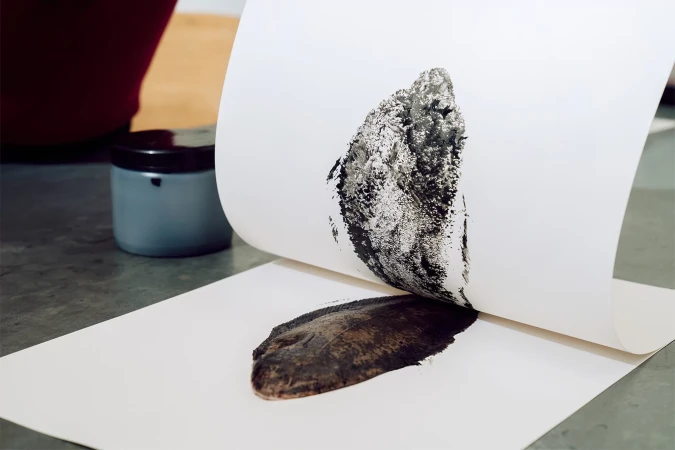 Monoprint artwork with dark brown and black ink pressing process on white paper, creating an abstract print with smudged texture.
