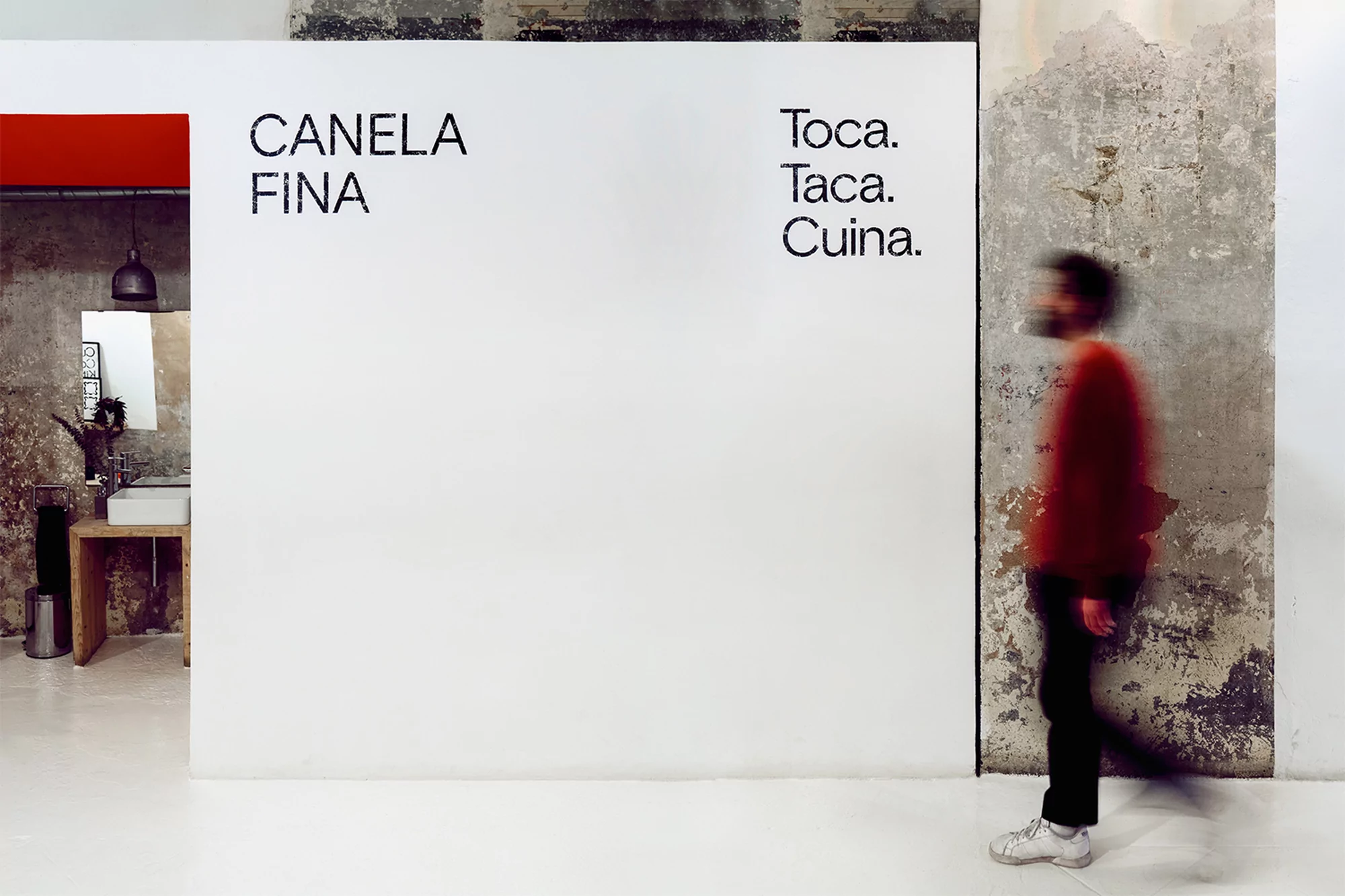 Blurred motion of an adult walking through an open doorway alongside a white wall with interior design text in an urban environment.