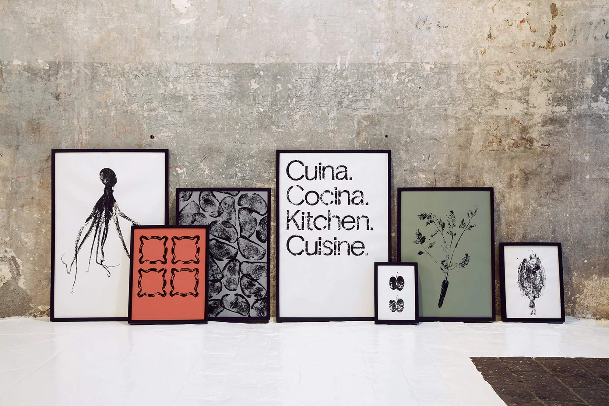 Black framed art prints feature an octopus, kitchen phrases, abstract shapes, vegetables, and a bird on a white floor against a grey wall.