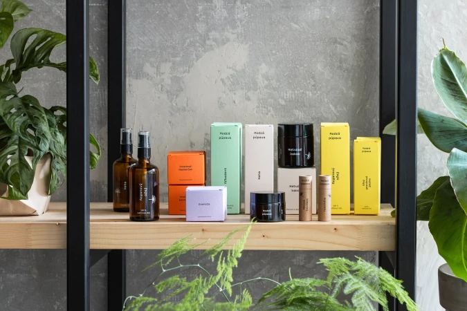 Collection of colorful skincare bottles and boxes arranged on a wooden shelf against a grey concrete wall.