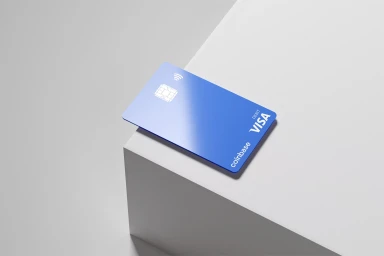 A blue Coinbase debit card resting on a white geometric podium under clean studio lighting.
