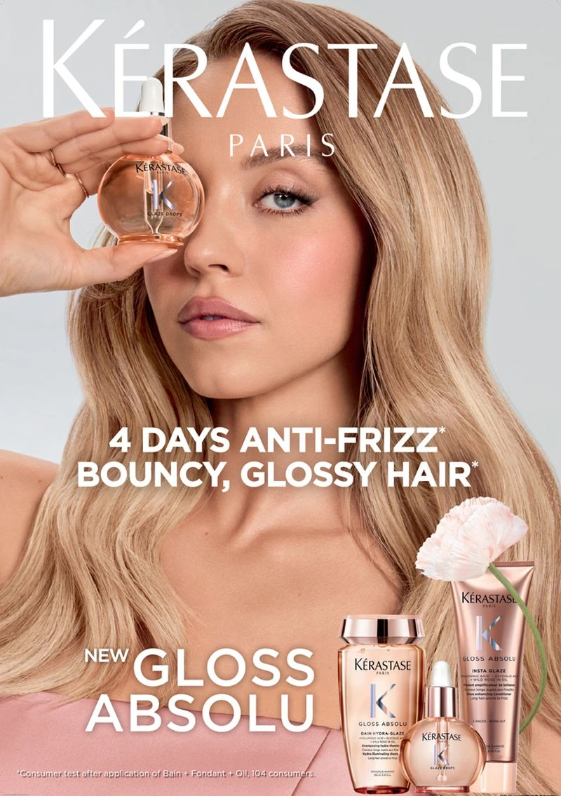 Sydney Sweeney holding a Kerastase Gloss Absolu serum bottle near her face in a beauty campaign advertisement.