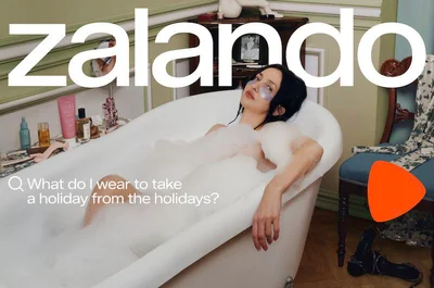 Woman with black hair reclining in a bubble-filled white bathtub inside a domestic bathroom setting with green walls.