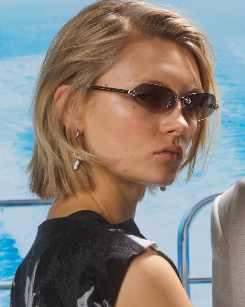 Close-up shot of a blonde woman with sunglasses on a yacht in front of blue water wearing a black and white sleeveless top and earrings.