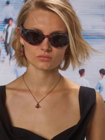 Close-up portrait of a blonde woman wearing plaid cat-eye sunglasses and a dark necklace for Vivienne Westwood Eyewear.