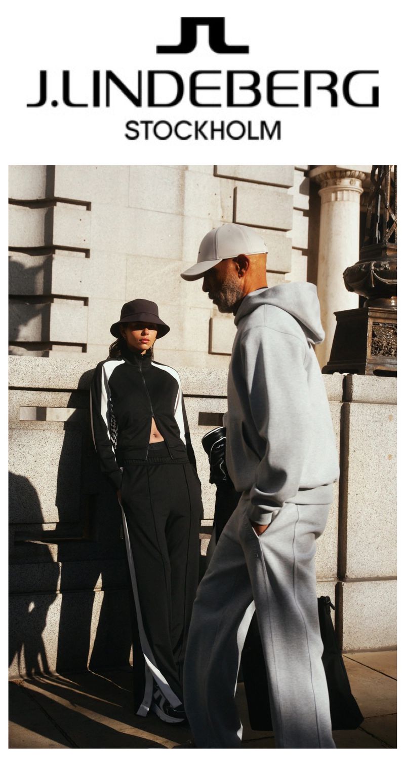 Two people stand in sunlight wearing tracksuits, with the J.Lindeberg Stockholm logo visible above them on the building.