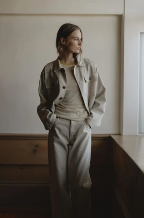 Indoor portrait of a female fashion model wearing matching beige jacket and pants, looking away from the camera near a window.