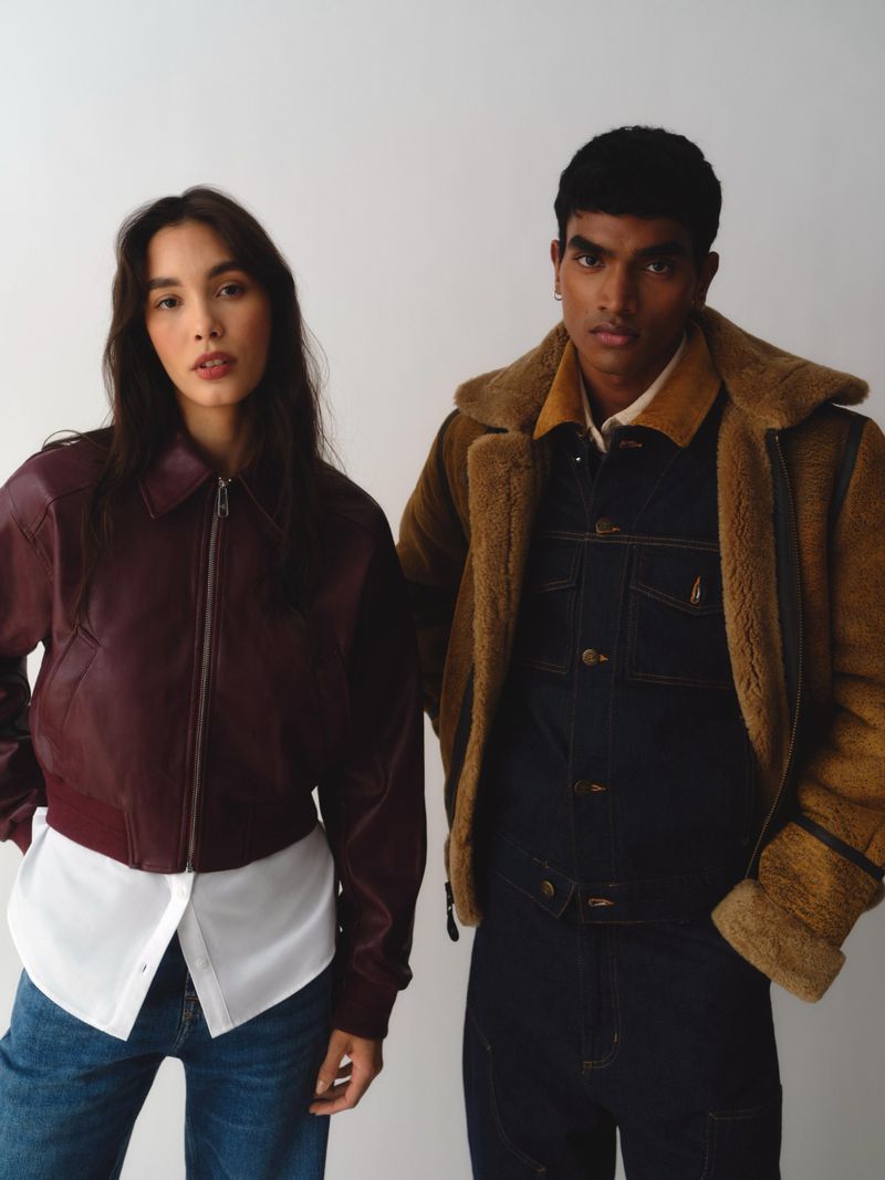 Two fashion models posing against a neutral white background wearing layered outerwear and denim