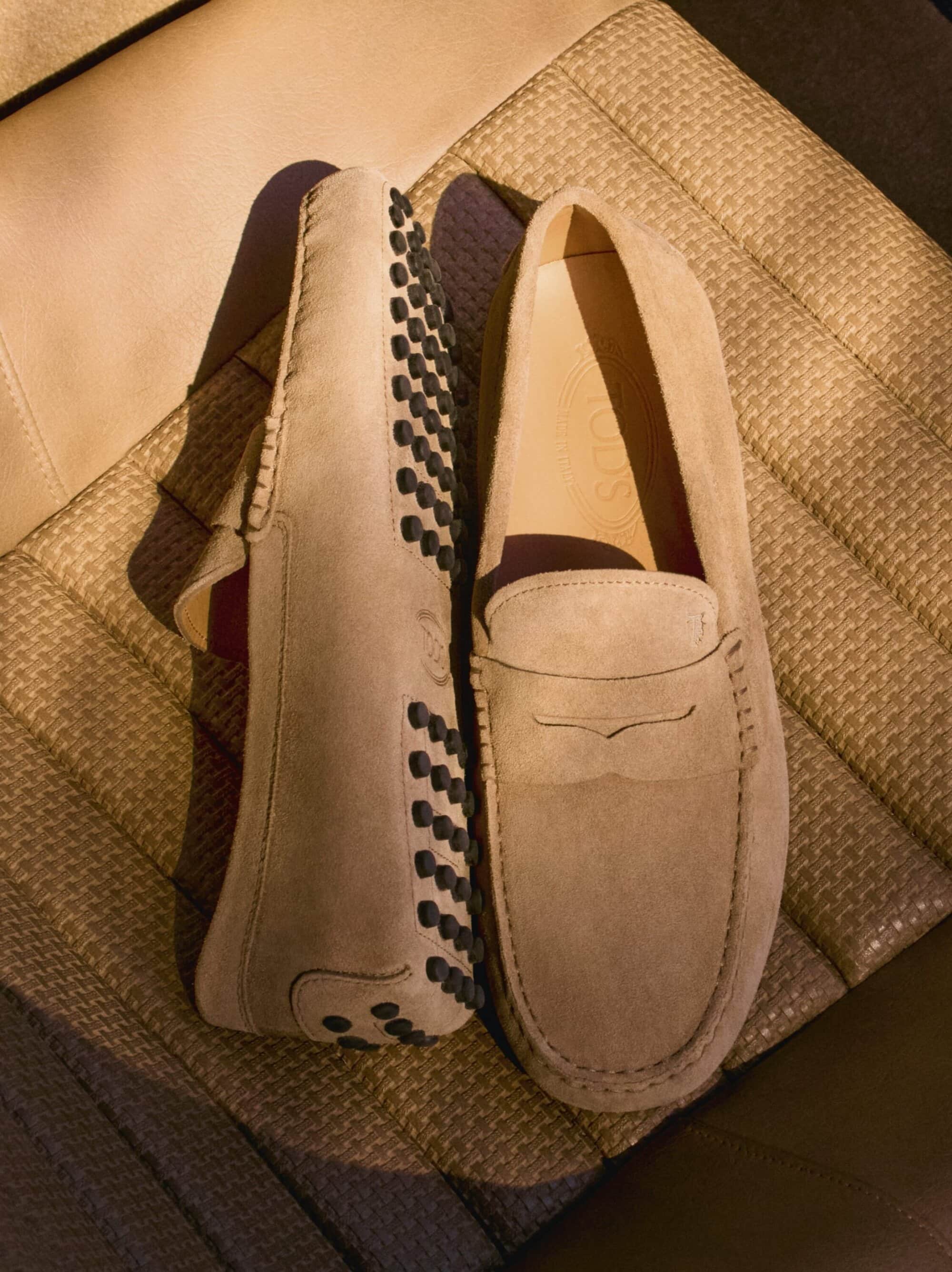 Close-up of two suede loafers in a tan color, showcasing the textures and design details of the footwear on a textured background.
