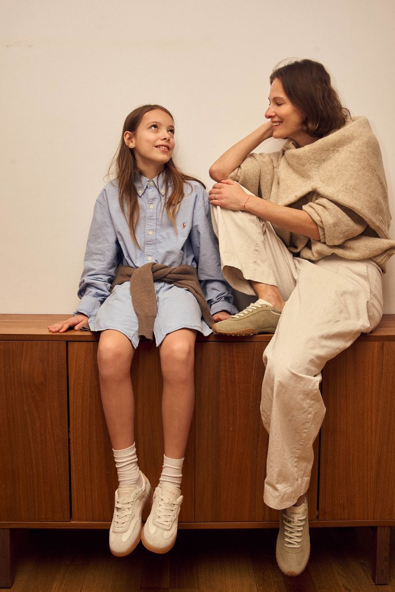 Indoor shot of a preteen girl and adult woman sitting on a cabinet, both wearing casual clothing, with the girl looking up at the woman.