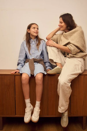 Indoor shot of a preteen girl and adult woman sitting on a cabinet, both wearing casual clothing, with the girl looking up at the woman.