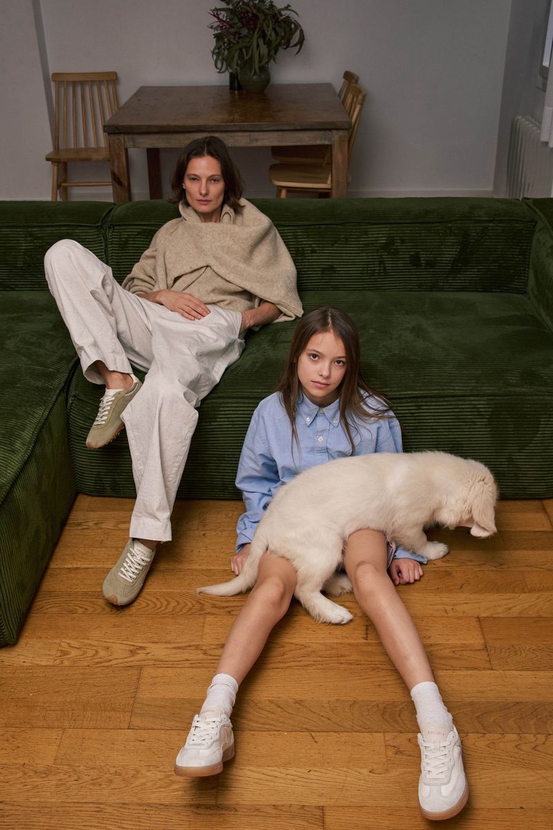 Indoor fashion shot of an adult and child on a green couch with a white puppy on child's lap, wooden floor, good light.
