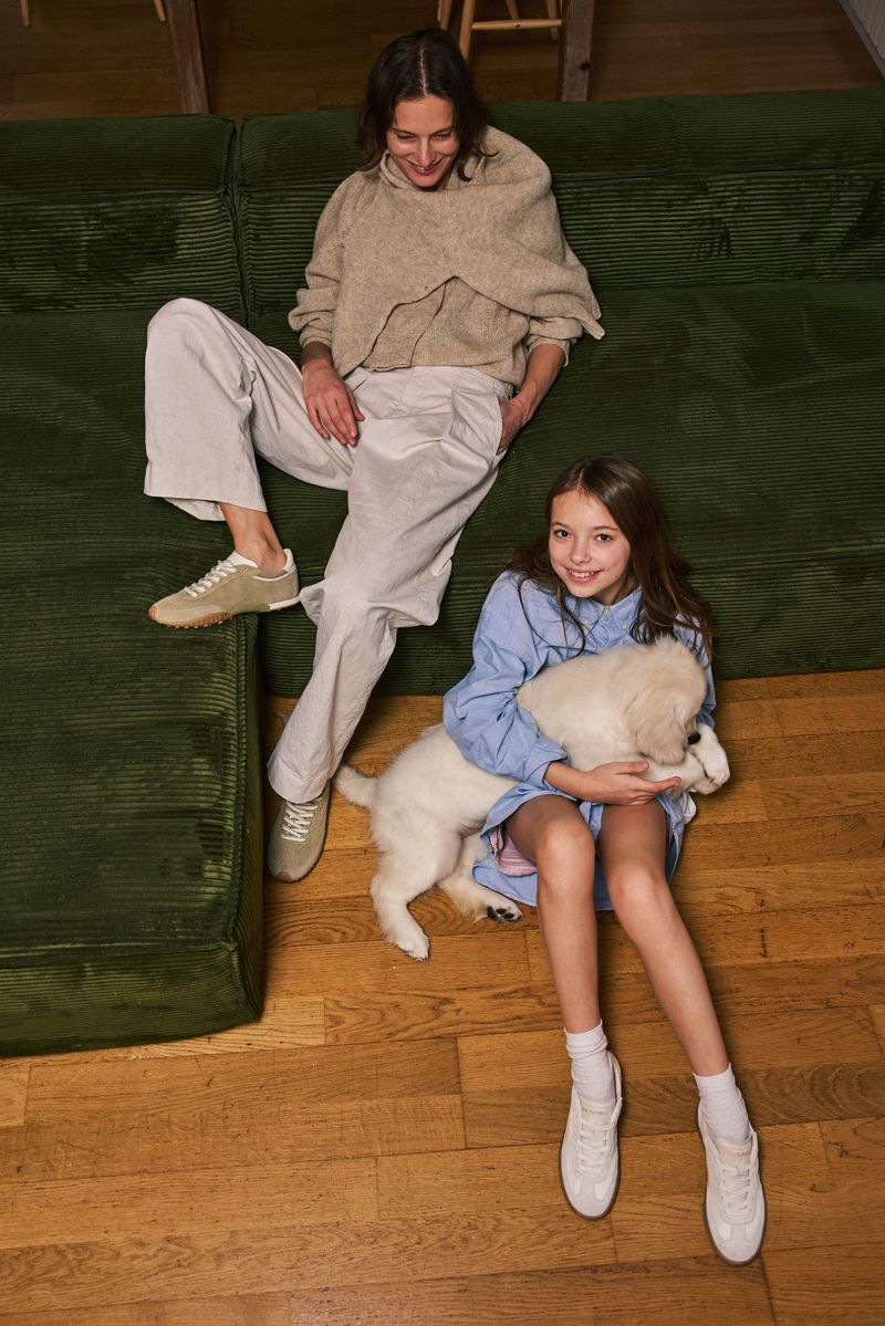 Mother and daughter are together inside, the daughter is holding a white puppy, top-down view, casual outfits, family time, indoor setting.