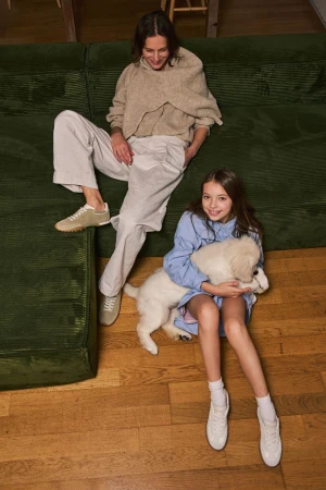 Mother and daughter are together inside, the daughter is holding a white puppy, top-down view, casual outfits, family time, indoor setting.