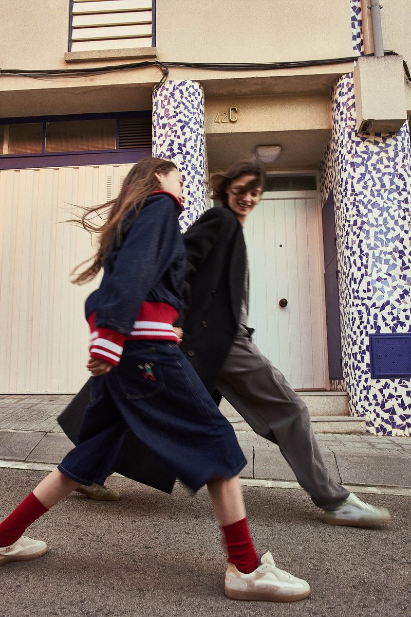 Two people walk side-by-side in a city street with a building featuring a unique blue-and-white tile facade, captured in eye-level shot.