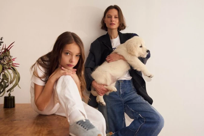 A mother in a blazer holds a Golden Retriever puppy while posing next to a young girl on a wooden table against a plain white backdrop.