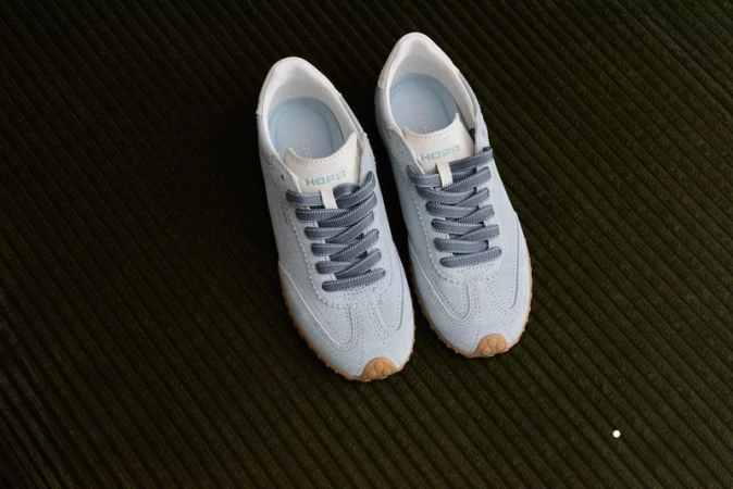 A pair of light blue suede sneakers with gray laces is displayed on a dark green corduroy surface, showcasing a minimalist aesthetic.