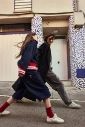 Two women walking outdoors past a tiled building facade in a campaign for HOFF photographed by Vitalik Melnikov.