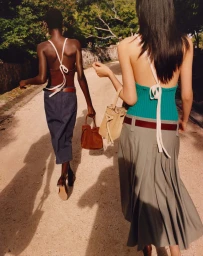 Two models walking away along a sunny dirt path wearing halter tops and carrying handbags for Tory Burch Spring 2026 ad campaign.