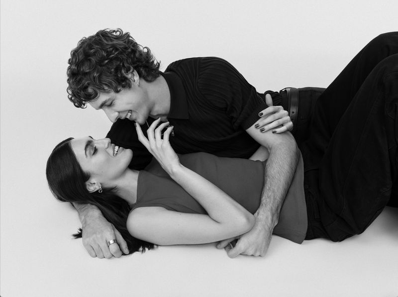 Black and white photo of a smiling couple laying together on the floor, looking into each other's eyes in a bright studio setting.