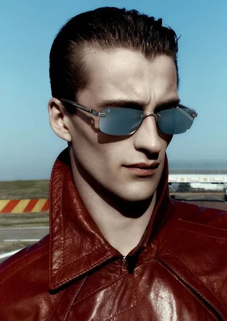 Close-up portrait of a male model wearing sunglasses and a red leather jacket outdoors against a clear blue sky.