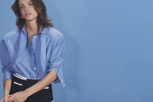 Model in blue striped shirt and black skirt against a blue studio backdrop for Maje S/S 26 campaign