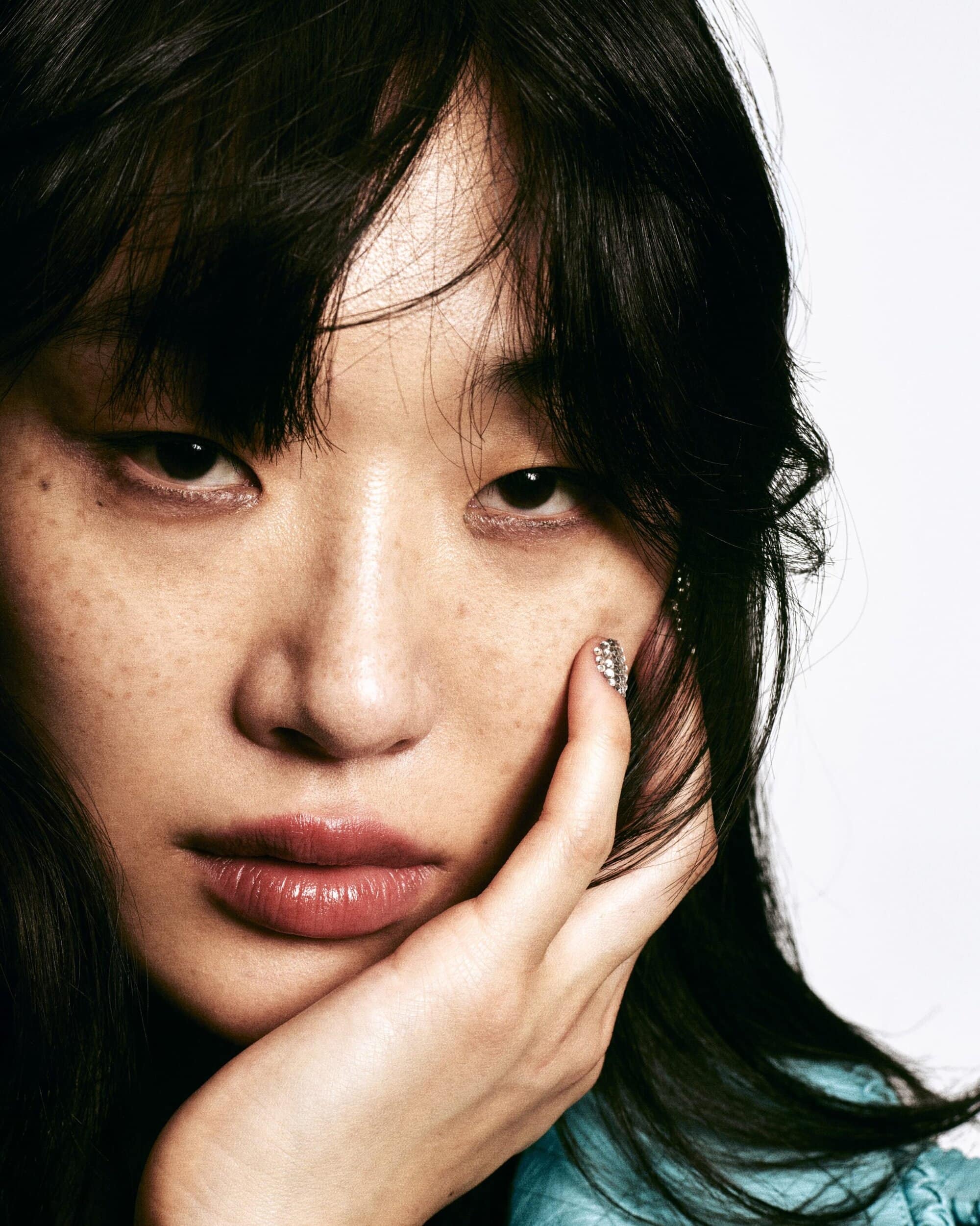 Close-up portrait of an adult female with dark hair and light skin. She is holding her face and wearing a blue top.