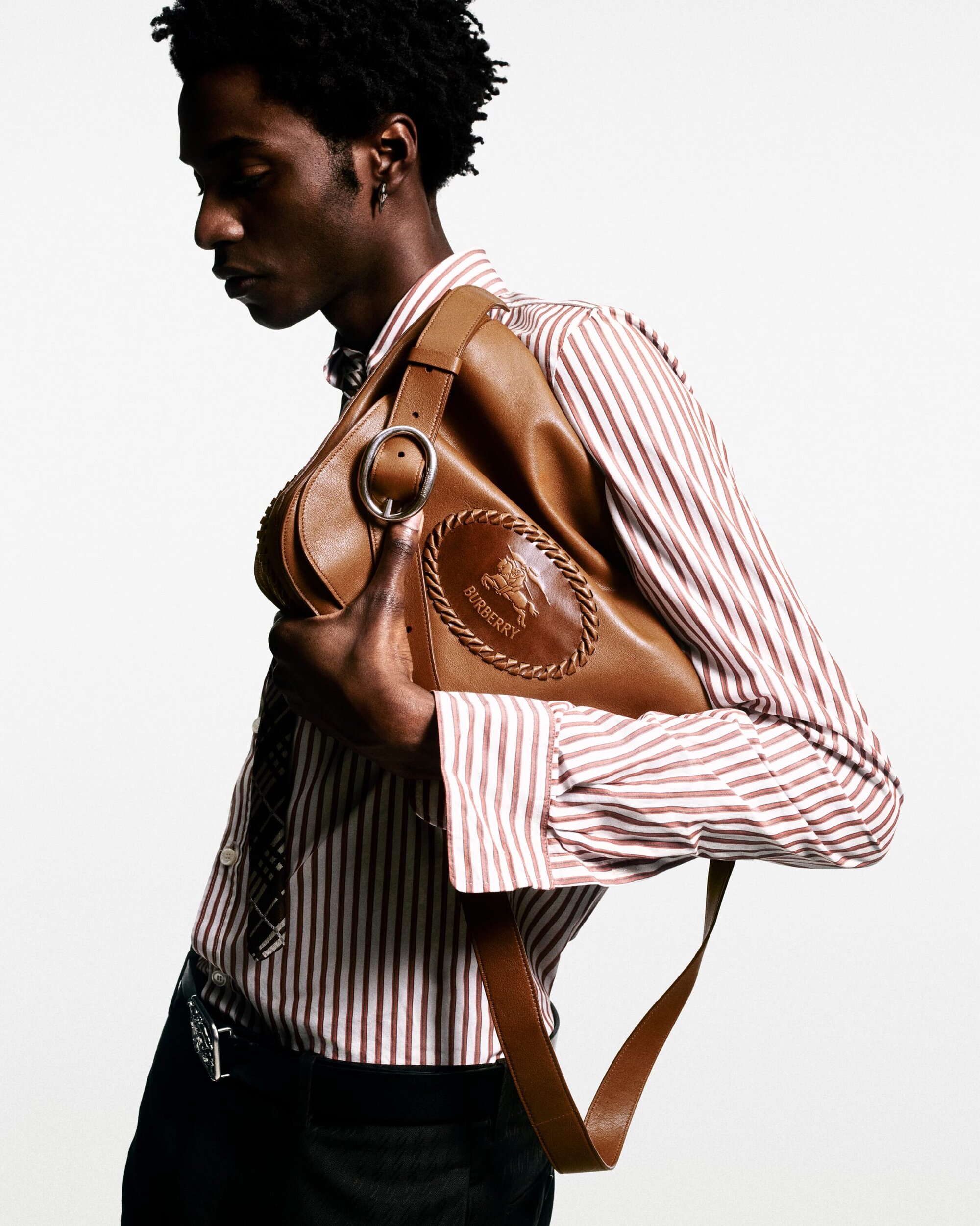 Model wearing a striped shirt and holding a tan leather shoulder bag against a plain white background