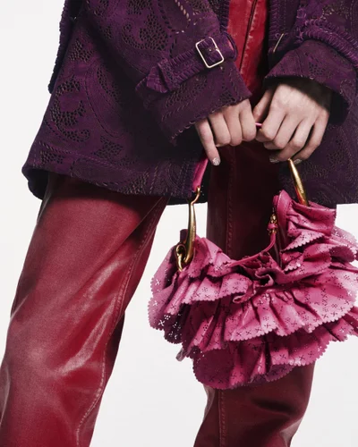 Close-up of a person wearing a purple textured coat and red leather trousers holding a pink ruffled handbag for Burberry.