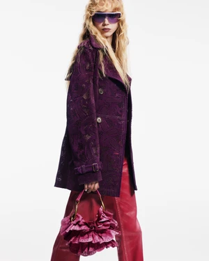 Model wearing tinted sunglasses and a purple lace trench coat holding a ruffled pink handbag against a plain white background.