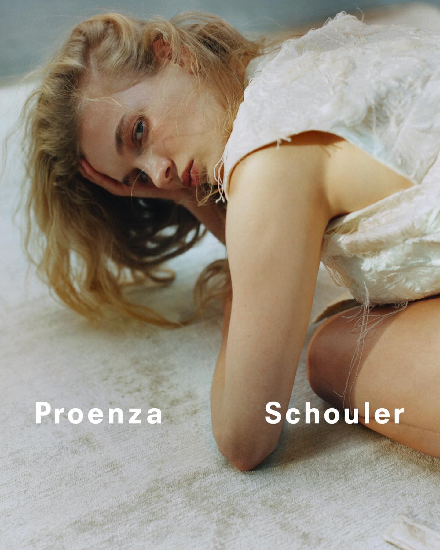 Fashion shot featuring a model with light blonde hair in an off-white dress in a reclined pose on a textured neutral background.