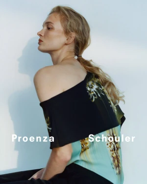 Model with blonde hair tied back wearing a black and teal patterned top against a white background