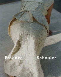 Model wearing a textured cream-colored sculptural garment shot from behind on a concrete surface for Proenza Schouler