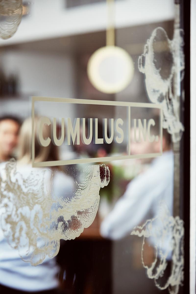 A view through a glass door with the words 'Cumulus Inc.' printed on it, with people visible inside a bright, indoor setting.