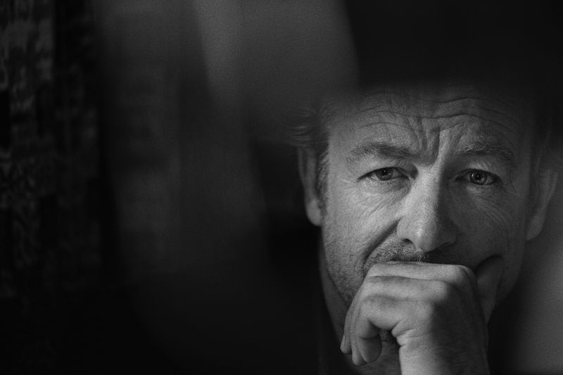 Dramatic black and white portrait of an adult man with a hand to his face, rendered with soft lighting and shallow depth of field.