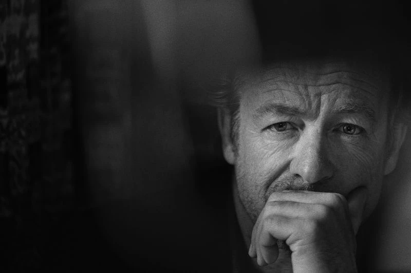 Dramatic black and white portrait of an adult man with a hand to his face, rendered with soft lighting and shallow depth of field.