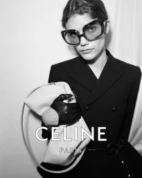 Model wearing dark sunglasses and black blazer holding a light handbag for Celine Summer 2026 Campaign