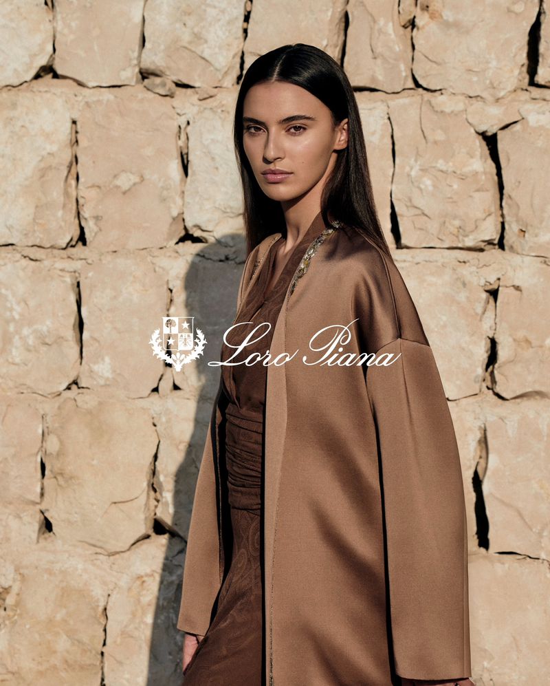 Elegant woman in bronze satin duster poses against a textured stone wall, showcasing high-fashion styling and neutral color palette.