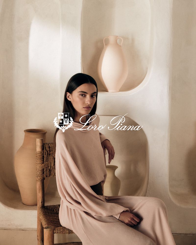 Elegant woman in soft pink loungewear sits on a wooden chair in a minimalist studio with neutral tones, pottery, and natural light.